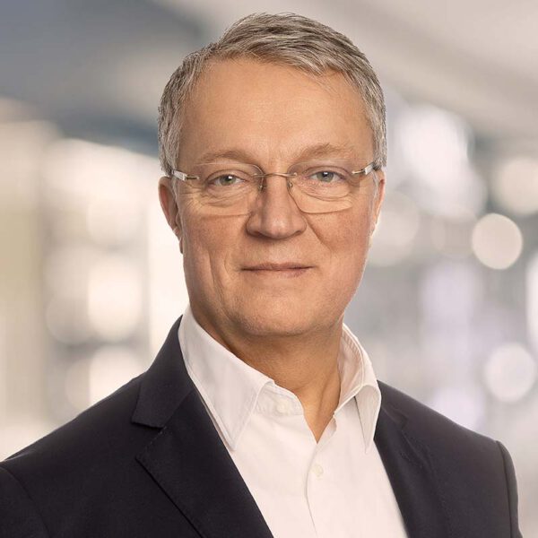 Porträt eines Mannes mit Brille, weißem Hemd und dunklem Sakko.