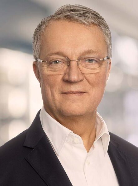 Porträt eines Mannes mit Brille, weißem Hemd und dunklem Sakko.